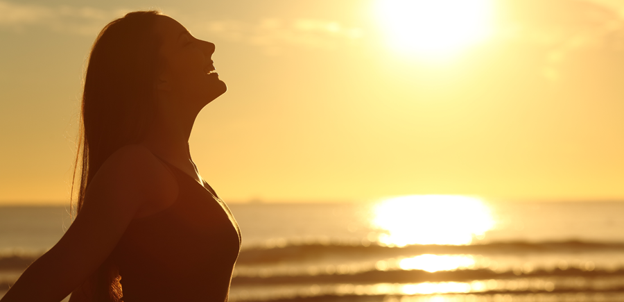 woman taking a deep breath near the ocean at sunset